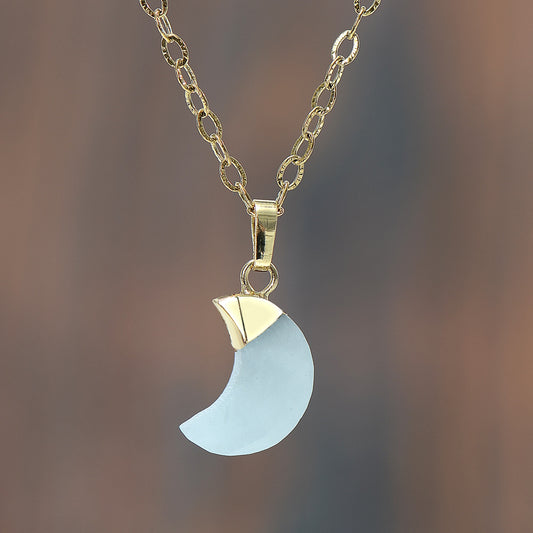 Necklace with a gold chain and a blue crescent moon pendant on a blurred background